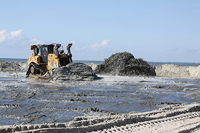 bulldoxer moving sand piped onto the beach