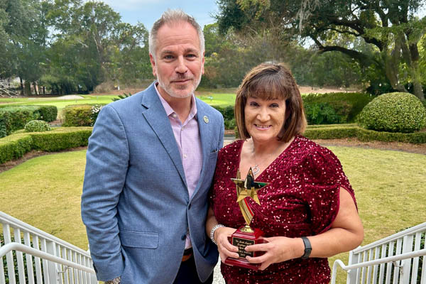 Faidra Smith holdng award standing outside next to Marc Orlando