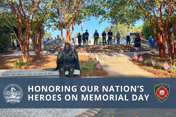 Bronze statue of soldier on a contrete bench with people in the background facing the Veterans Memorial